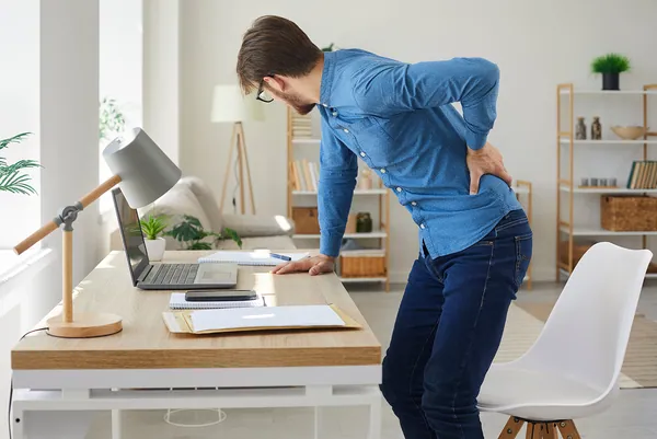 Man holding his lower back in pain at his desk